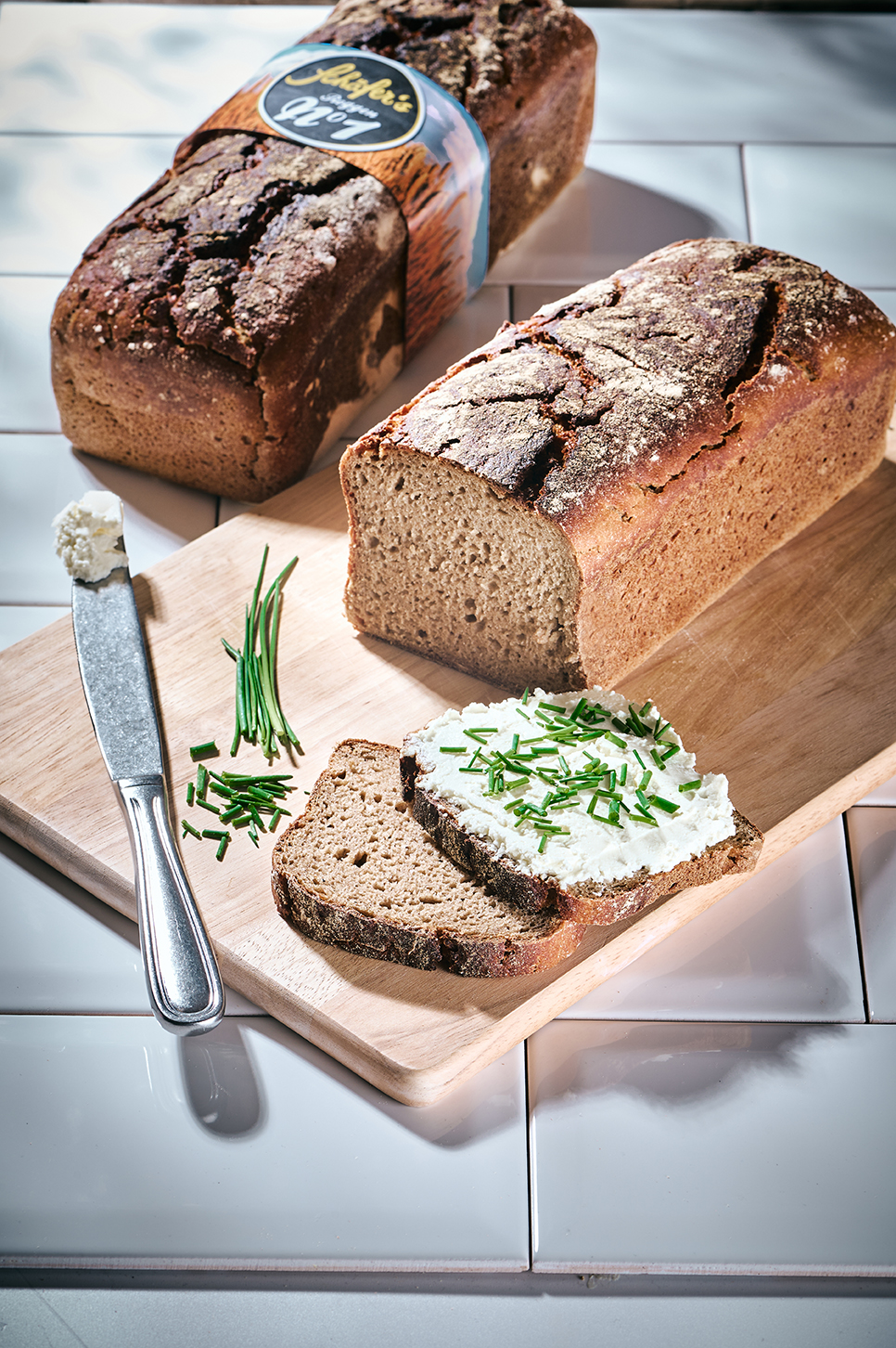 Laib Schäfer’s Roggen No. 1 Brot auf einem Holzbrett, angeschnitten mit zwei Brotscheiben