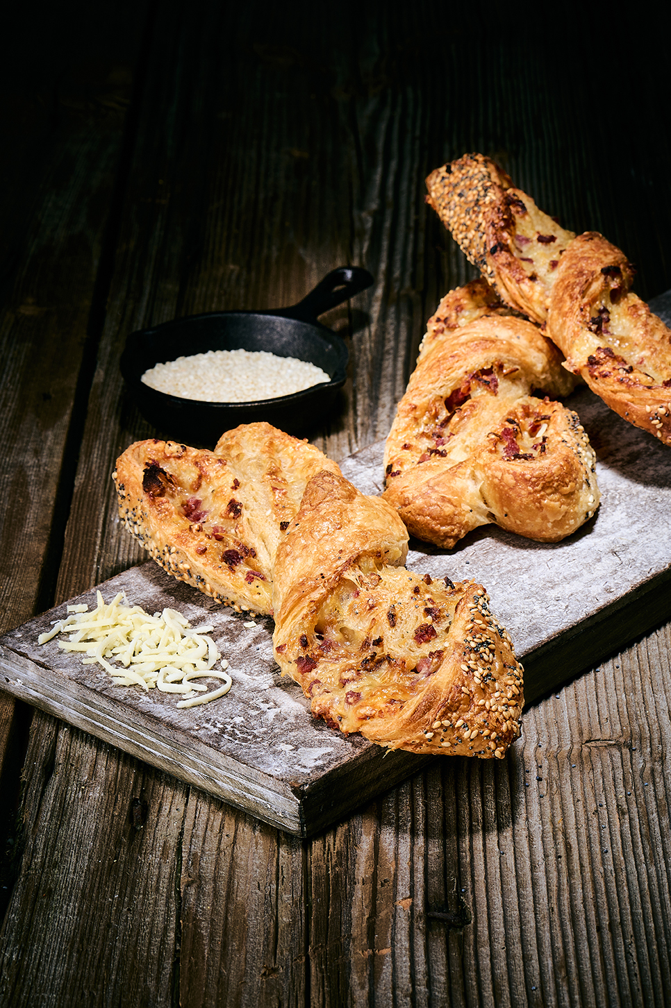 Blätterteigstangen mit Käse, Speckwürfeln und Sesam auf Holzbrett