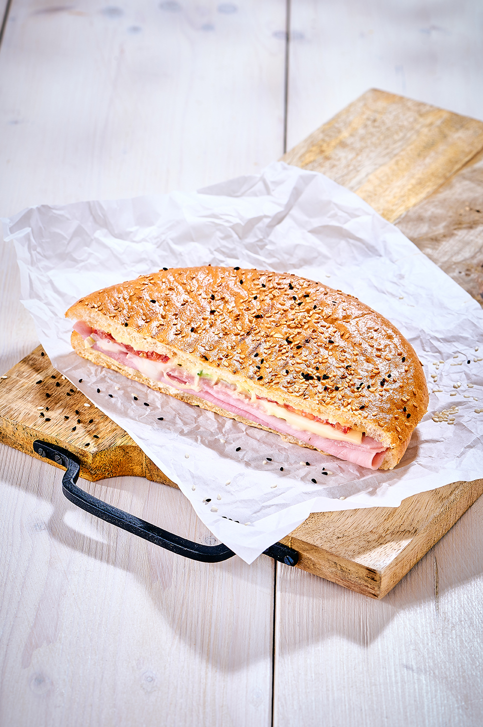Gefülltes Fladenbrot mit Schinken, Käse, Tomate, Gurke und Sesam auf Backpapier