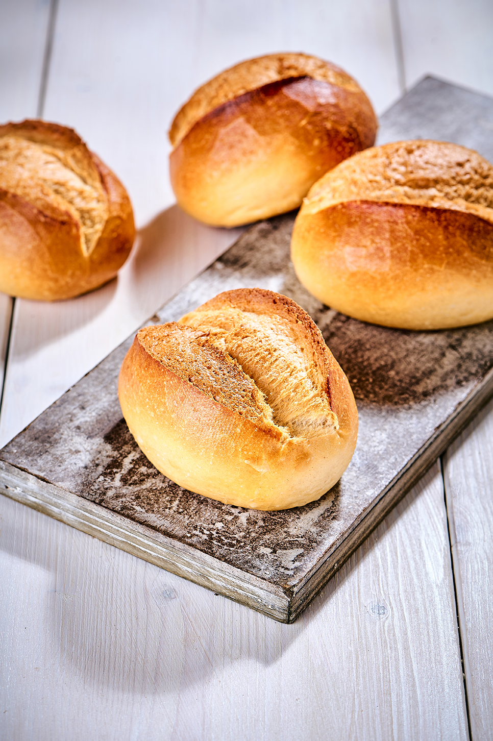 Vier frisch gebackene Brötchen auf einem Holzbrett, mit goldbrauner Kruste und weichem Inneren.