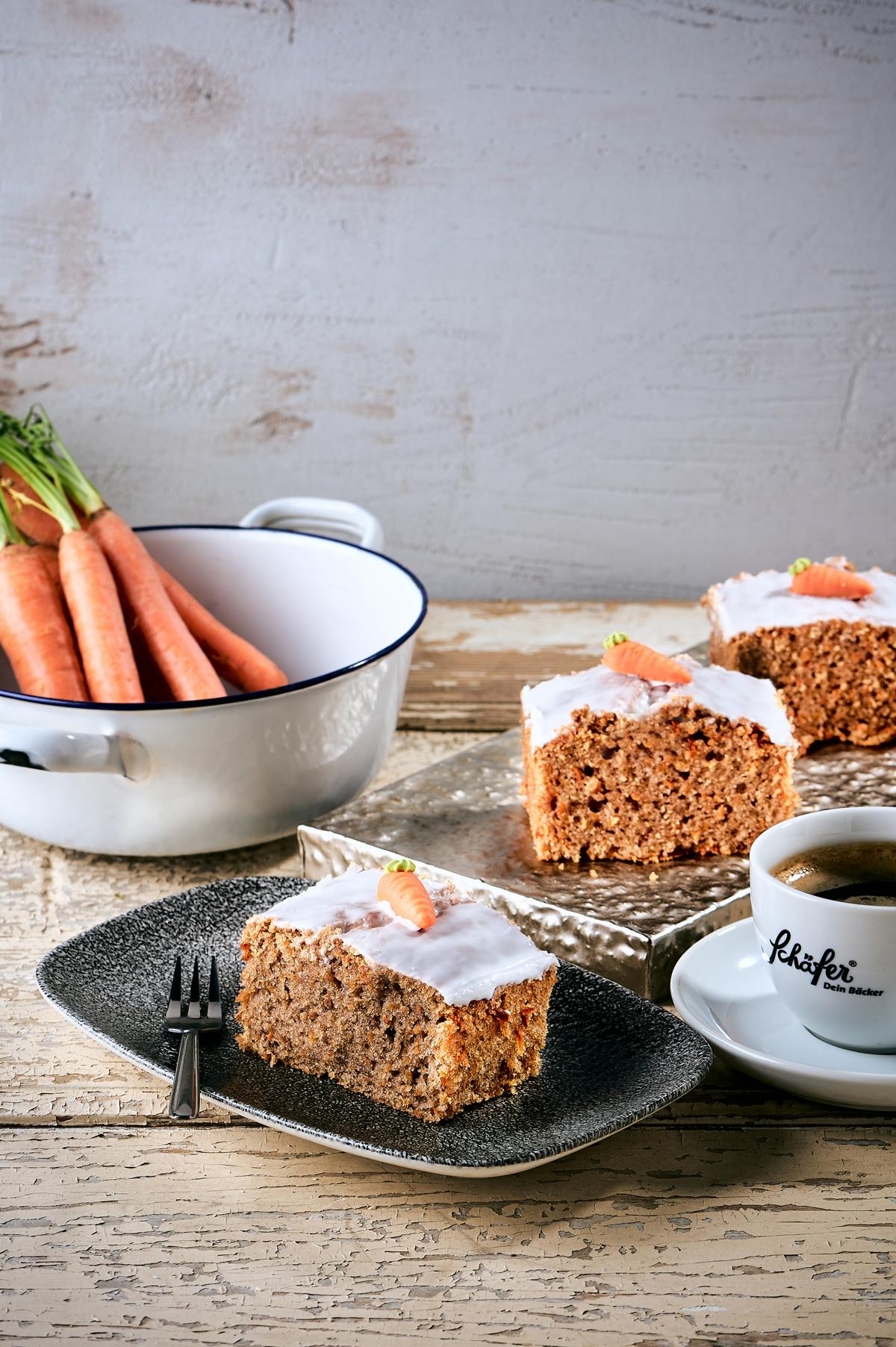 Stück saftiger Karottenkuchen mit Zuckerglasur und Marzipankarotte neben Kaffee