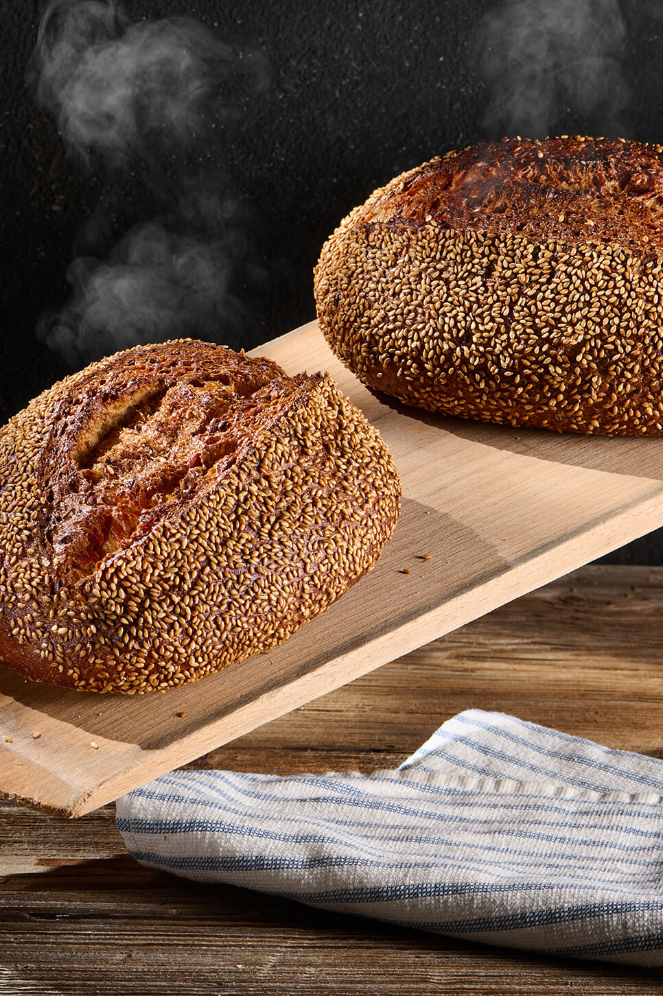Dinkelvollkornbrot mit Sonnenblumenkernen und Frischkäse auf Holzbrett, daneben Körner.
